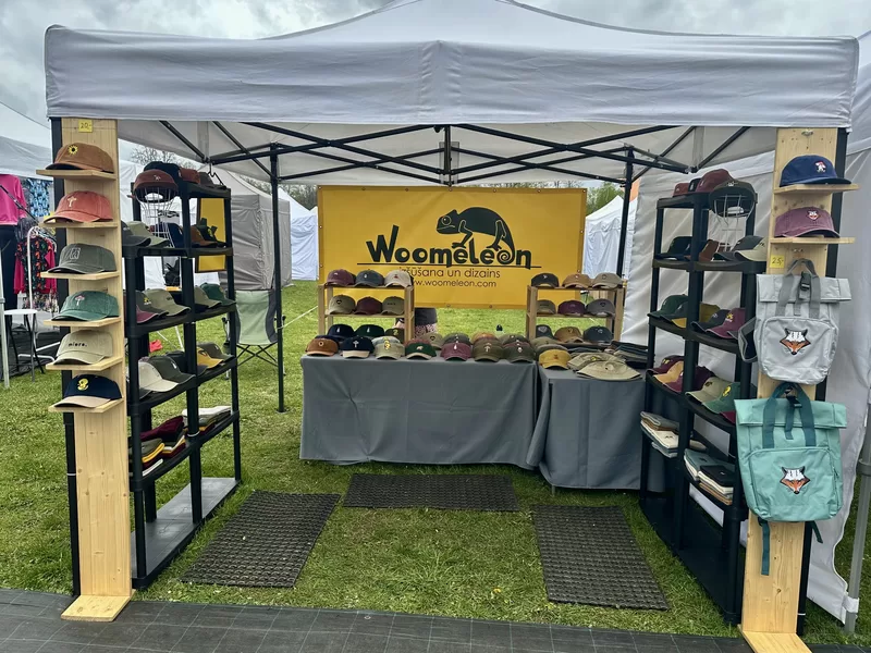 Woomeleon market stall displaying embroidered caps on black pastic shelves with yellow brand banner